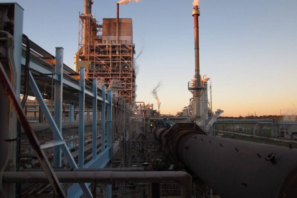 Industrial processing facility at sunset with visible emissions and large ductwork, illustrating complex air pollution control needs such as the venturi wet scrubber.